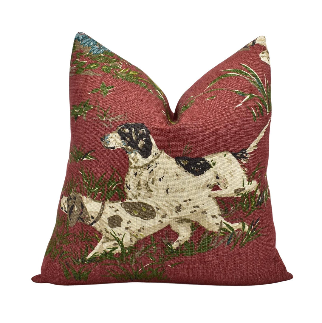 a red pillow with a printed design of two dogs, one white and one brown, running through a grassy area.